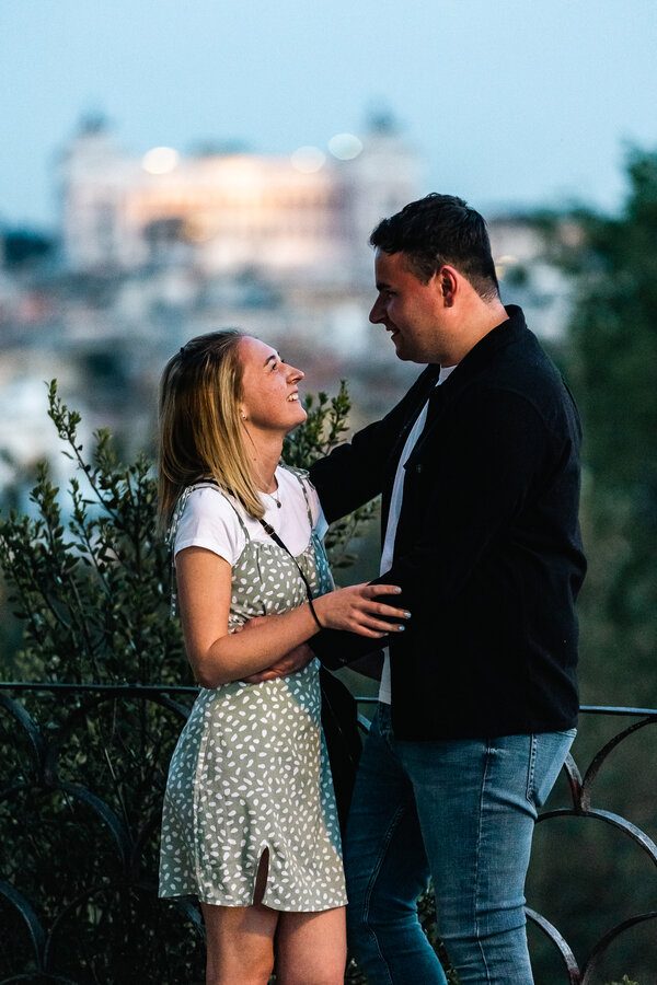 Happy newly-engaged couple looking at each other with Rome in the background on the Pincian Hill in Rome at the blue hour