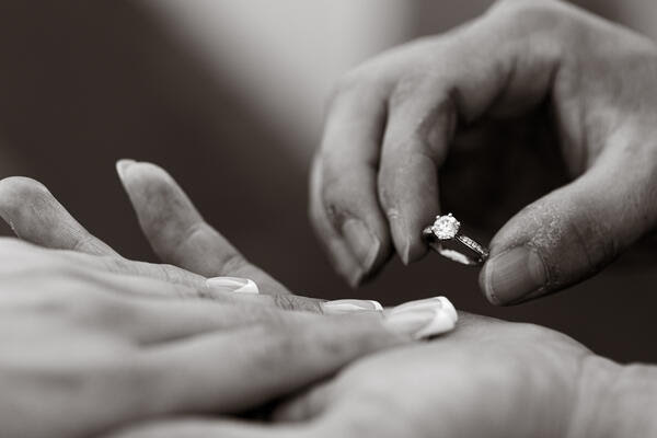 Black and white image of fiancé holding the engaement ring next to his fianceé's hand