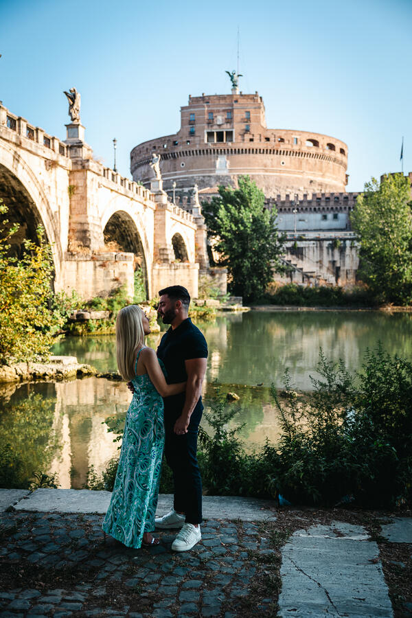 Newly-engaged couple holding each other with Castel Sant'Angelo in the background during their surprise marriage proposal in Rome