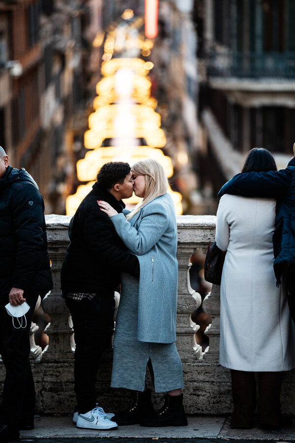 Newly-engaged couple kissing with the Via del Corso in the background lit with Christmas lights