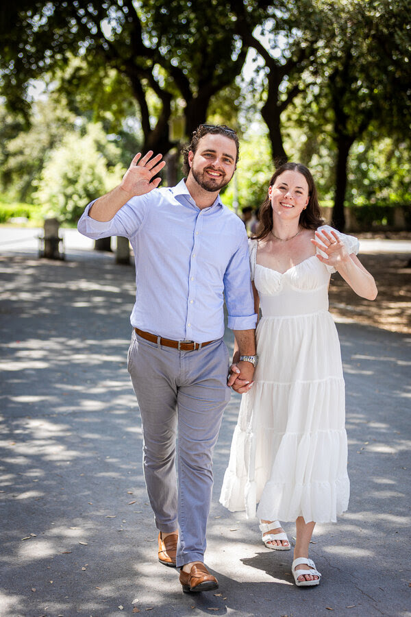 Happy newly-engaged couple waiving good-bye during their surprise marriage proposal photoshoot at the Pincio Gardens in Rome