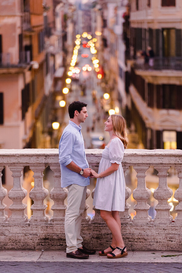 newly-engaged couple holding hands at the Spanish Steps with Via Condotti in the background after sunset