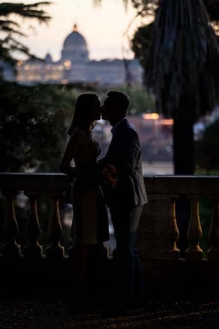 Newly-engaged couple kissing with the Vatican in the background at dusk