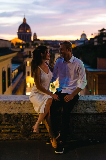 Newly-engaged couple during their engagement photo session looking at each other after sunset with Rome as a backdrop