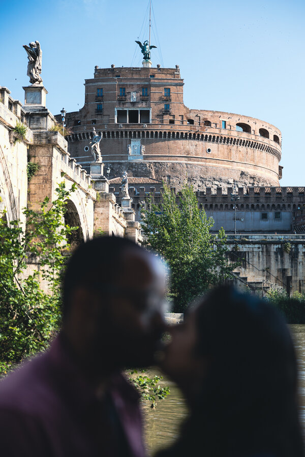 Newly-engaged couple kissing with Castel Sant'Angelo in the background during their surprise wedding proposal shoot in Rome