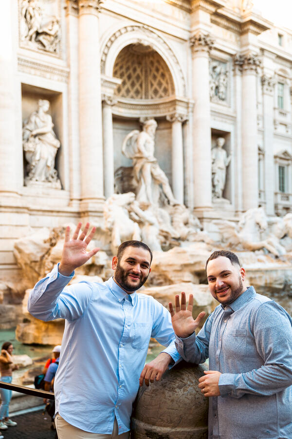 Newly-engaged happy couple waving goodbye their same-sex surprise proposal photoshoot by the Trevi Fountain in Rome
