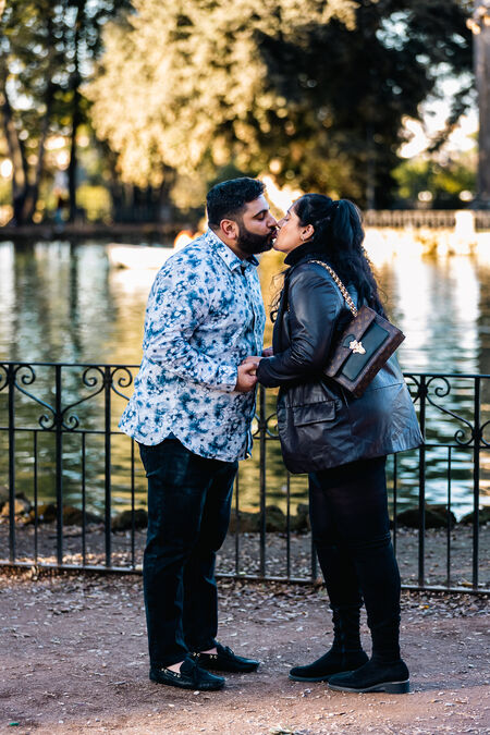 Newly-engaged couple kissing during their surprise wedding proposal photo session in Villa Borghese by the pond