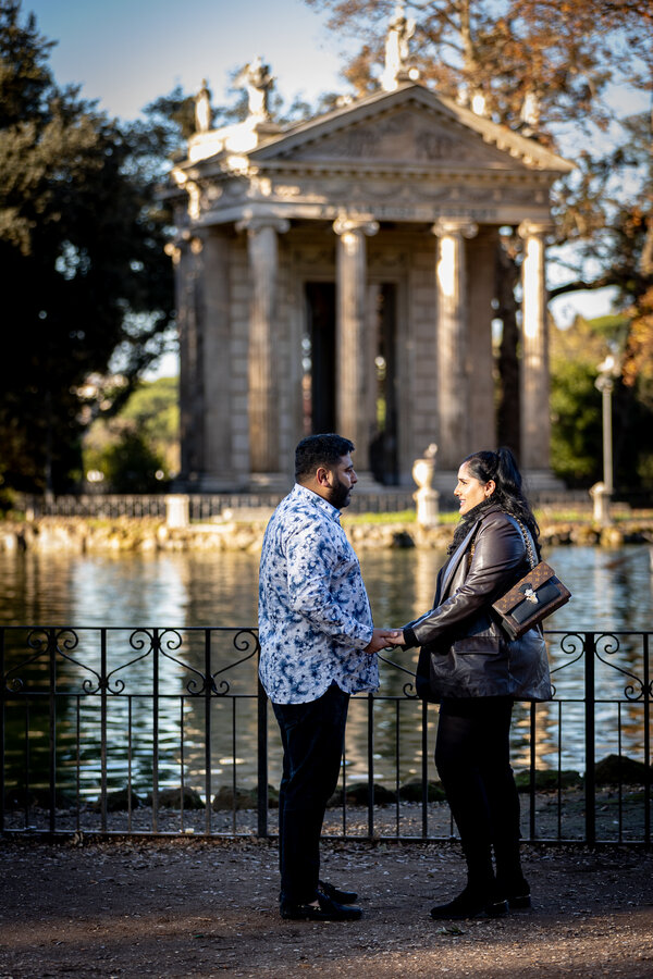 Man declaring his love to his girlfriend while holding her hands by the pond in villa borghese in Rome