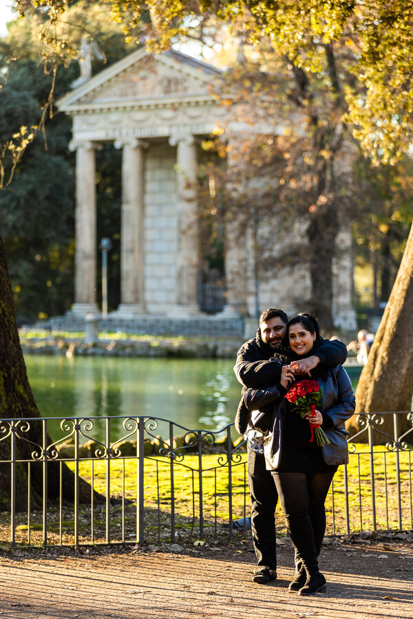 A happy newly-engaged couple by the pond in Villa Borghese during their surprise marriage proposal photo shoot in Rome