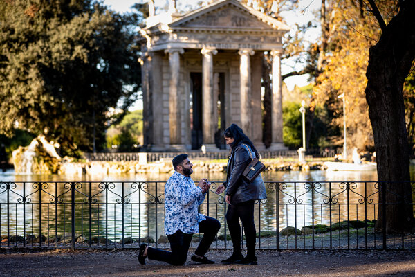 Man offering the engagement ring to his girlfriend by the pond in Villa Borghese during his surprise wedding proposal in Rome