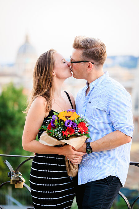 Newly-engaged couple kissing while holding a beautiful bouquet of colourful flowers on the Terrazza Belvedere in Rome