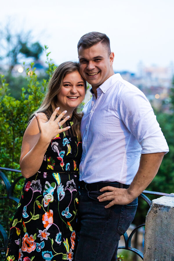 Happy newly-engaged couple smiling for the camera while the fiancé is showing off her new engagement ring in Rome