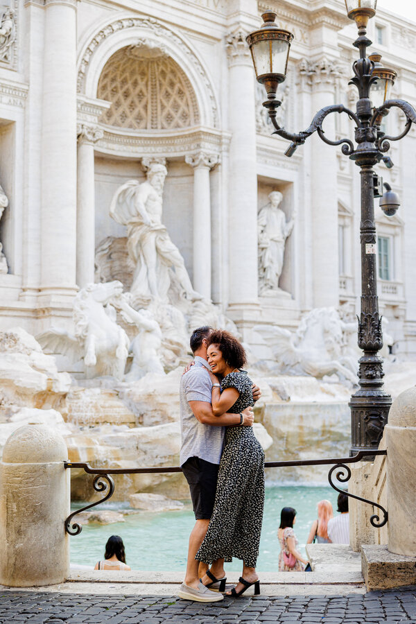 Newly-engaged couple hugging each other during their surprise marriage proposal photoshoot at the Trevi Fountain in Rome