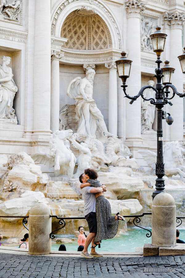 Happy newly-engaged couple jumping during their surprise wedding proposal photoshoot at the Trevi Fountain in Rome
