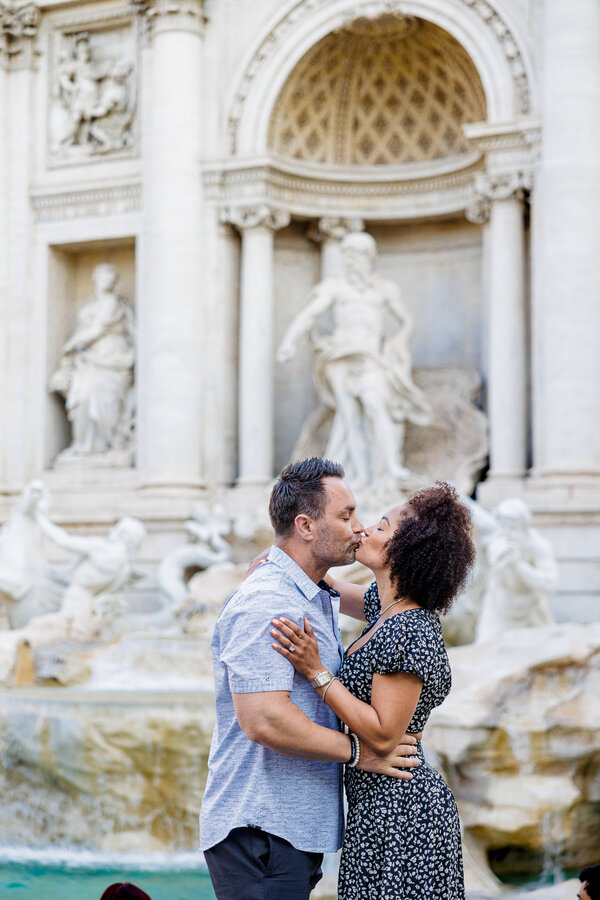 Newly-engaged couple kissing with the Trevi Fountain in the background in Rome
