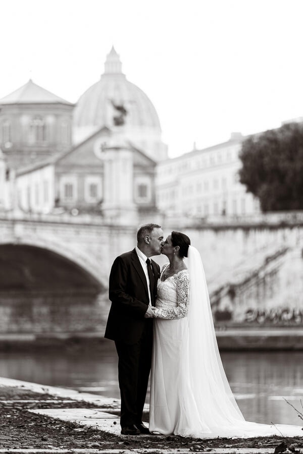 Black and white image of Sposi Novelli couple kissing on the Tiver riverbank in Rome