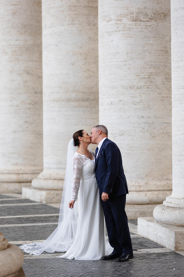 Sposi Novelli couple kissing under the colonnade in Saint Peter's square