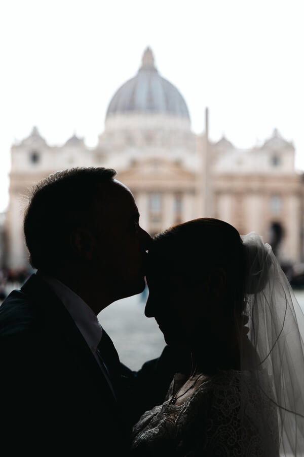 Newly-wed husband kissing his wife's forehead during their Sposi Novelli photoshoot in Via della Conciliazione in Rome