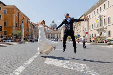 A happy shot of Novelli Sposi couple jumping in the air along Via della Conciliazione, Rome