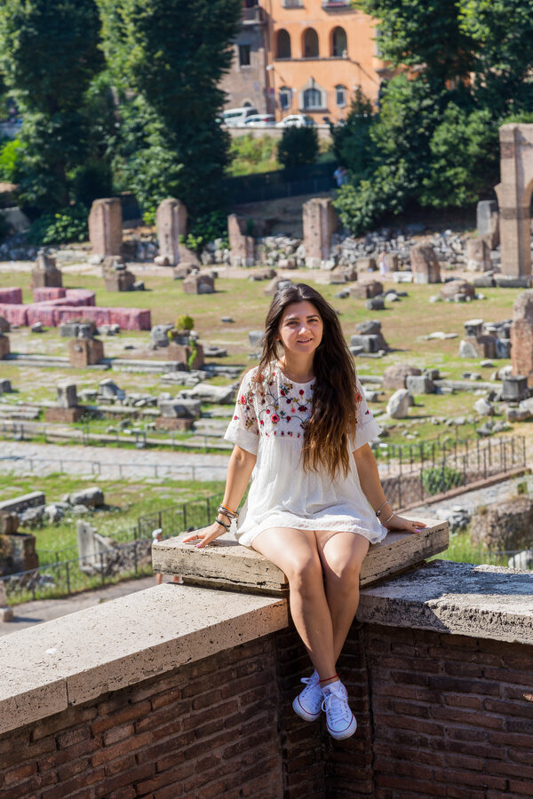 Girl in a white dress sitting on ledge with the Roman Forum in the background