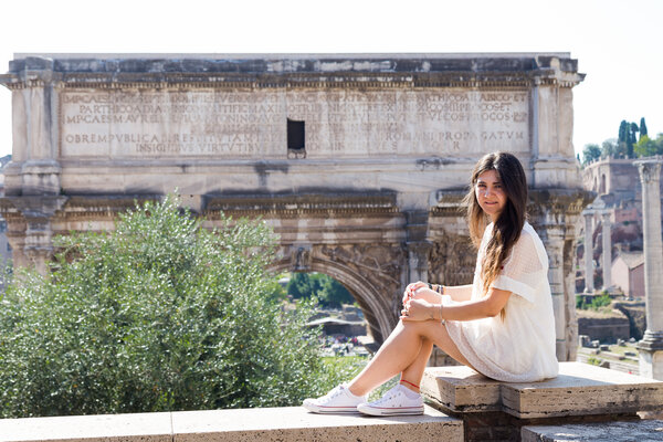Girl in a white dress sitting on ledge with the Septimius Severus Arch in the background