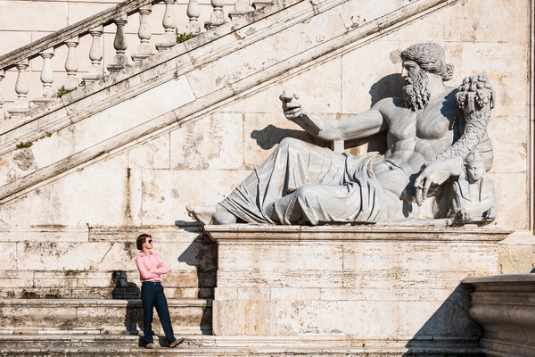 Boy standing at the foot of Nile River God statue on the Capitoline Hill during his senior photoshoot in Rome