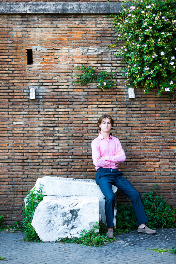 Boy sitting on white marble stone posing for the camera during his senior photoshoot in Rome
