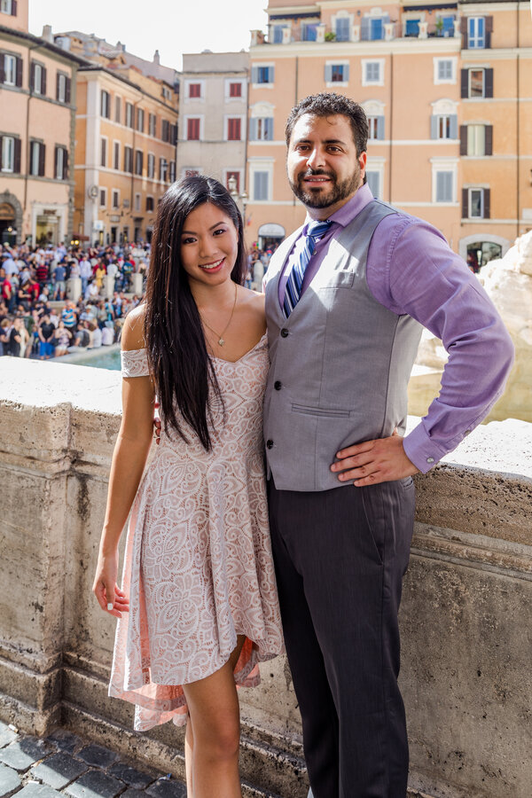 A stylish couple smiles at the camera on a warm and sunny day at the Trevi Fountain