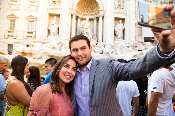 Beautiful and happy couple takes a selfie with the Trevi Fountain in the background durind their vacation photo session in Rome