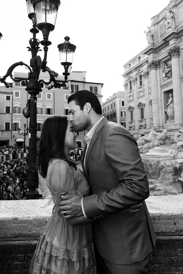 Black and white portrait of a husband kissing his wife on her forehead with the Trevi Fountain in the background