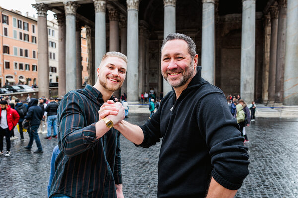 Father and son-in-law armwrestling during their family photo session in Piazza del Pantheon in Rome
