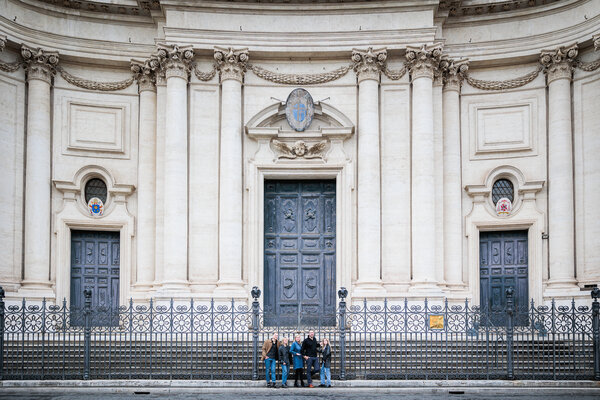 Landscape shot of family leaning against a church gate in Piazza Navona in Rome
