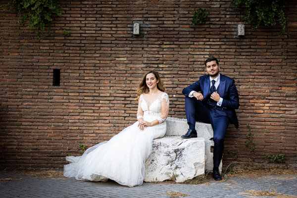 Portrait of wedding couple sitting a marble stone in Rome