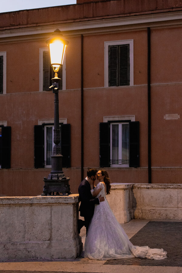Bride and groom kissing at night under a lamp post on the Spanish Steps in Rome