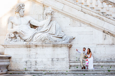 Wedding couple sitting next to the statue representing the Tiber River God on the Capitoline Hill in Rome