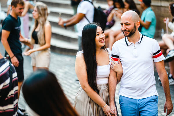 Happy newly-engaged couple walking by the Trevi Fountain during their engagement photo shoot in Rome