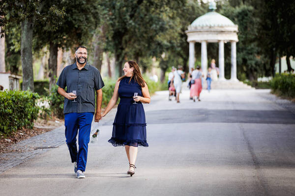 Couple strolling while drinking champagne during their Wedding anniversary photo shoot in Villa Borghese in Rome