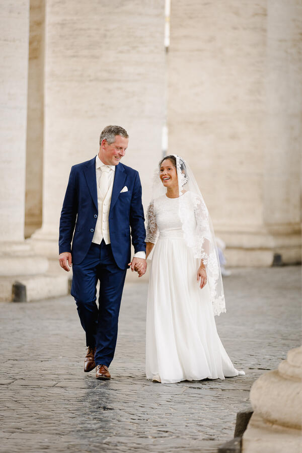 Sposi Novelli couple walking hand in hand under the colonnade in Saint Peter's Square